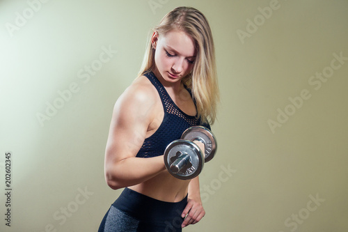 young woman blond doing exercises for the muscles of the hands with a dumbbell in the gym. the girl warmes up and goes in for sports