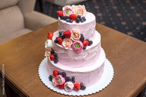 Three tiered pink wedding cake decorated with berries and flowers. Concept patisserie floristic from sugar mastic