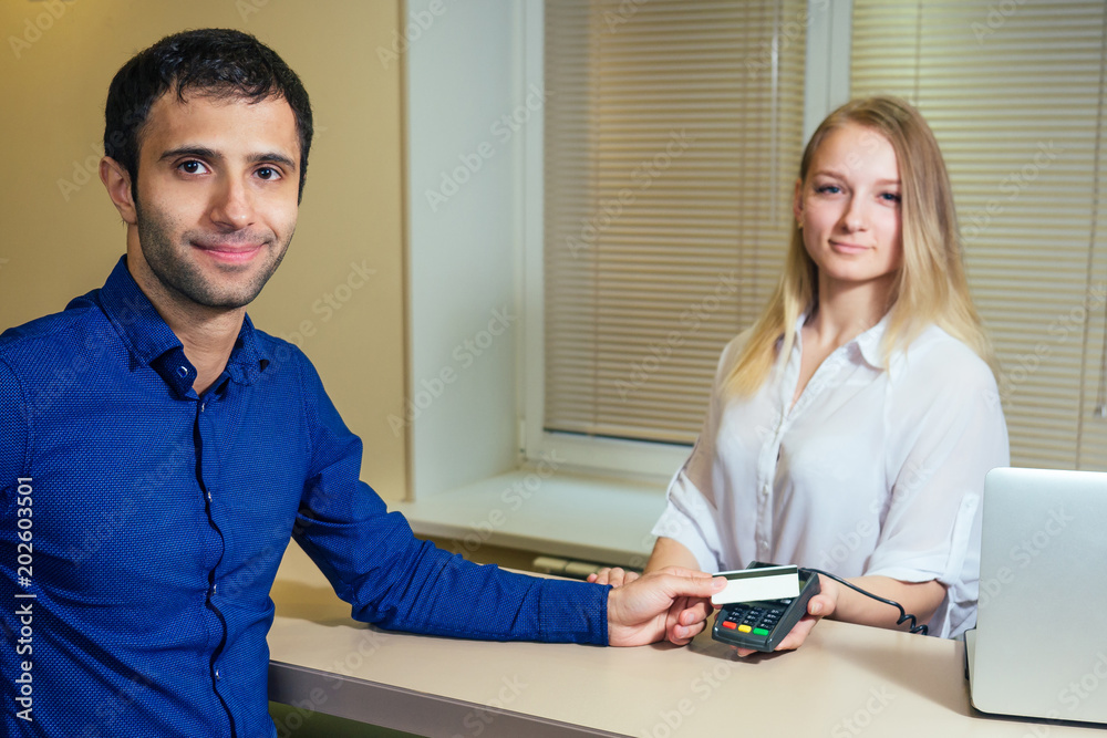young woman with a blonde is smiling with a man. credit card, girl, cash, credit and bank registration. reception in the hotel young woman with a blonde is smiling with a man. credit card, girl, cash, credit and bank registration. reception in the hotel