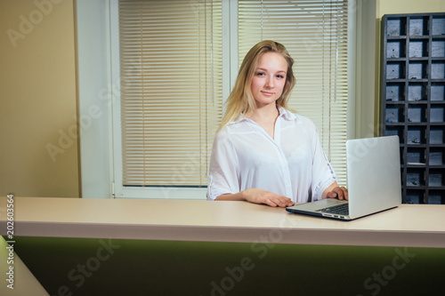 young blond woman smiling and looking at laptop with phone. reception in the hotel