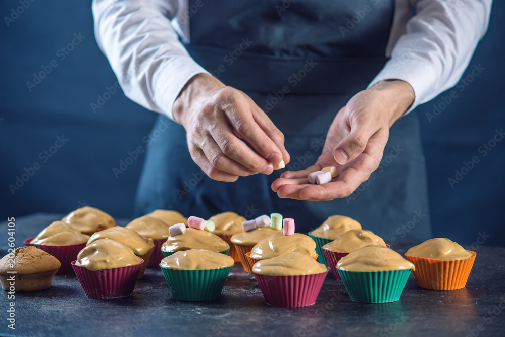 Chef in a black apron hands decorated cupcakes marshmallow. Concept of confectionery cooking