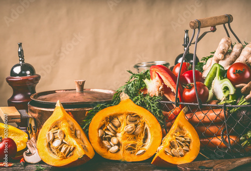 Hokkaido Pumpkins on kitchen table with cooking pot and ingredients at rustic wall background, front view. Healthy vegetarian  food and eating concept.  Autumn seasonal eating