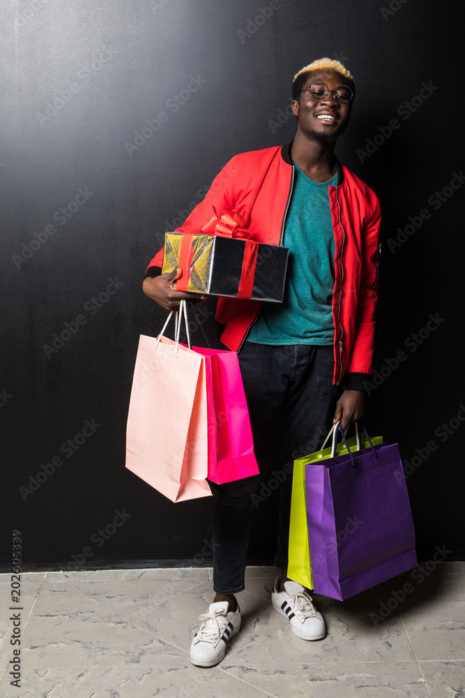 Φωτογραφία African American man with colorful paper bags and gift isolated on black backgro