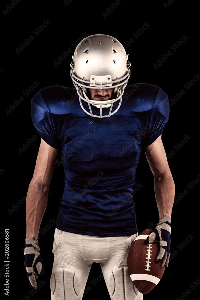 Confident American football player looking down against black