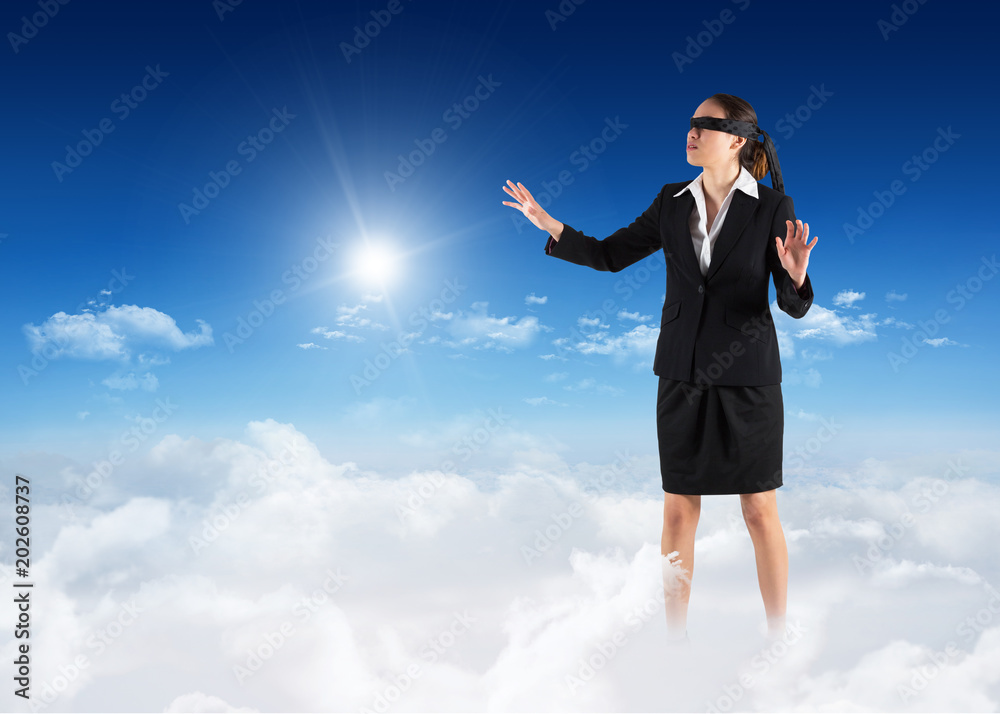 Blindfolded businesswoman with hands out against bright blue sky over clouds Blindfolded businesswoman with hands out against bright blue sky over clouds