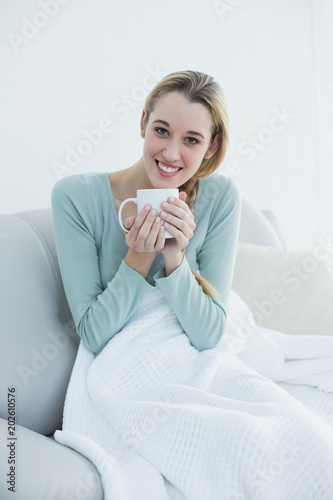 Pretty casual woman holding a cup sitting on couch under a blanket