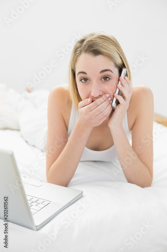 Portrait of attractive surprised woman phoning lying on her bed