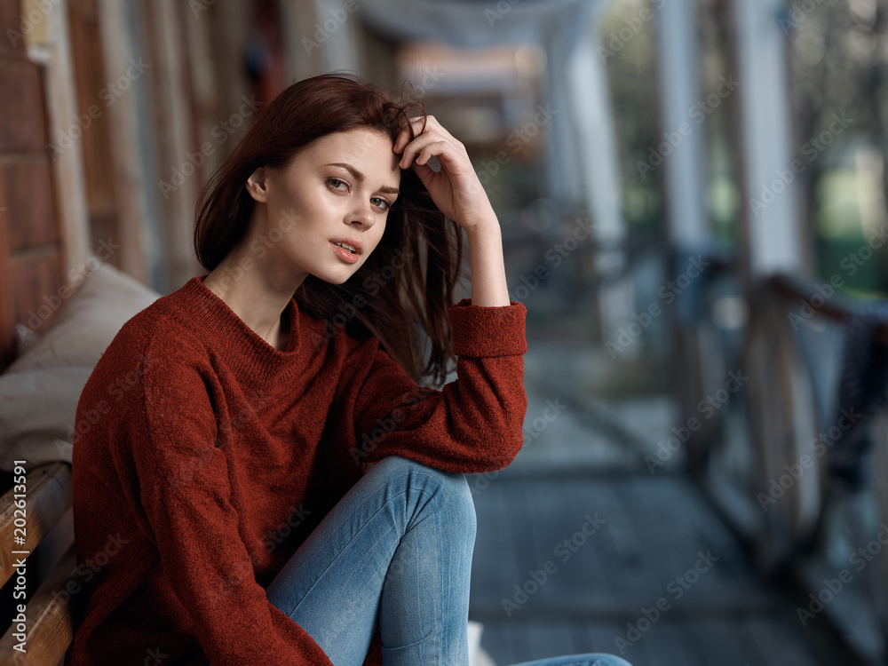 woman in jeans and jacket sitting on a bench near the building woman in jeans and jacket sitting on a bench near the building
