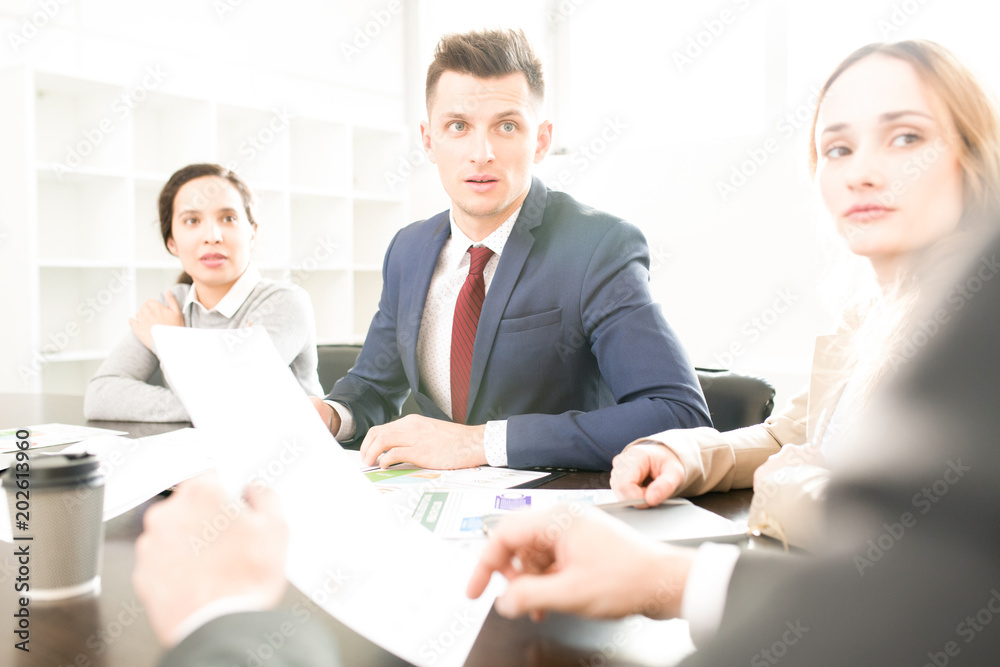 Serious curious company employees sitting in a row at table and listening to boss who explaining documentary at staff meeting Serious curious company employees sitting in a row at table and listening to boss who explaining documentary at staff meeting