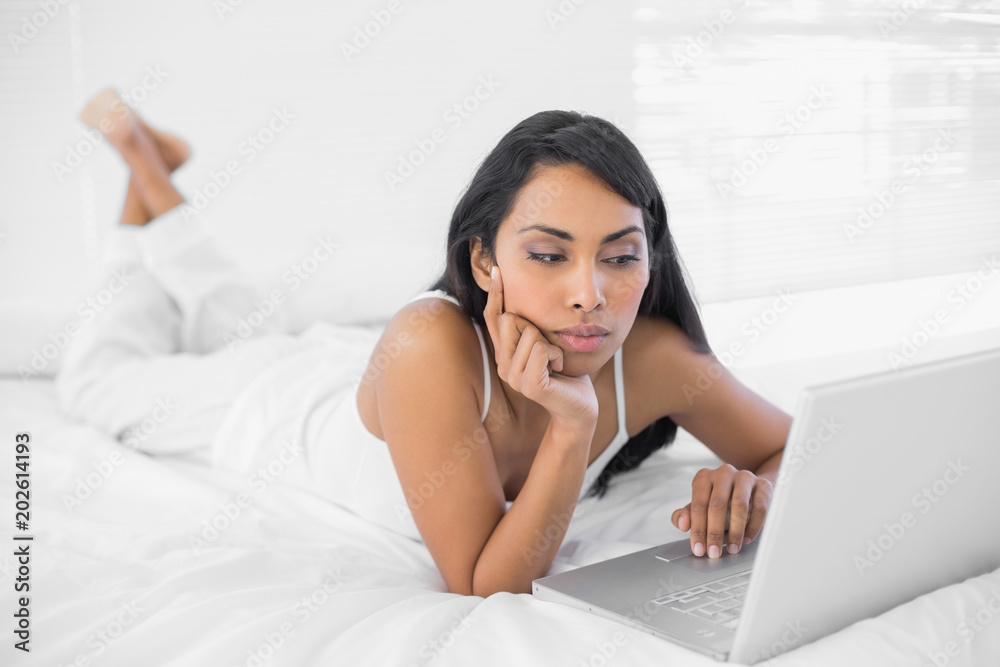 Cute thinking woman working on her notebook lying on bed Cute thinking woman working on her notebook lying on bed