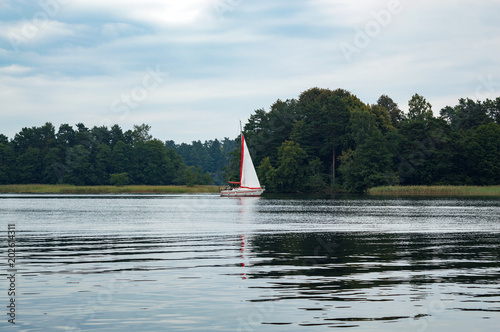 Photos Evening landscape with sailing boast on lake Galve with pine forest on the horiz