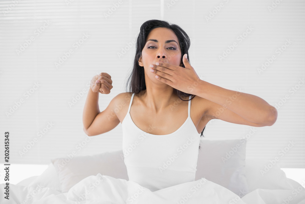 Attractive young woman stretching out and yawning while sitting on her bed Attractive young woman stretching out and yawning while sitting on her bed