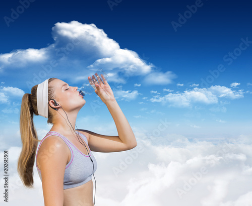 Sporty blonde drinking water against bright blue sky with clouds