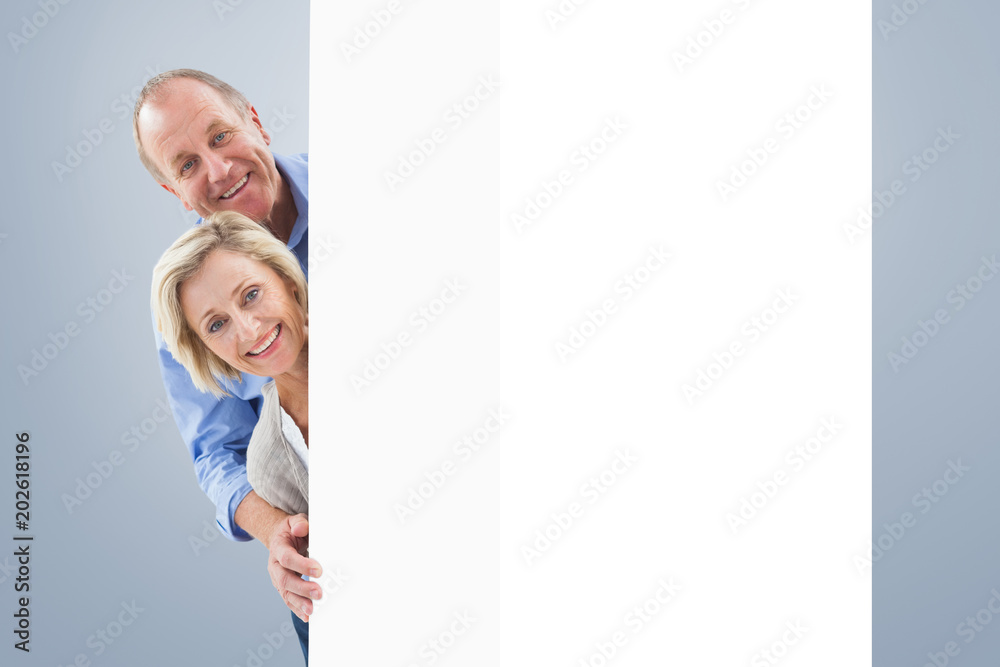 Mature couple smiling behind wall against grey vignette Mature couple smiling behind wall against grey vignette