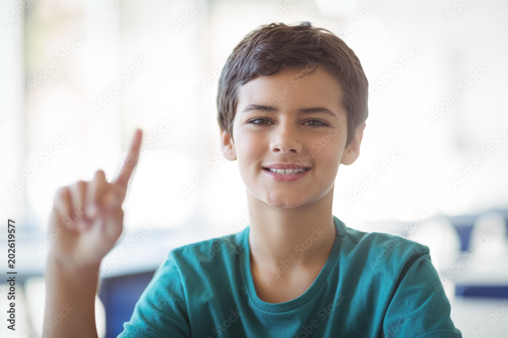 Portrait of happy schoolboy raising hand in classroom Portrait of happy schoolboy raising hand in classroom
