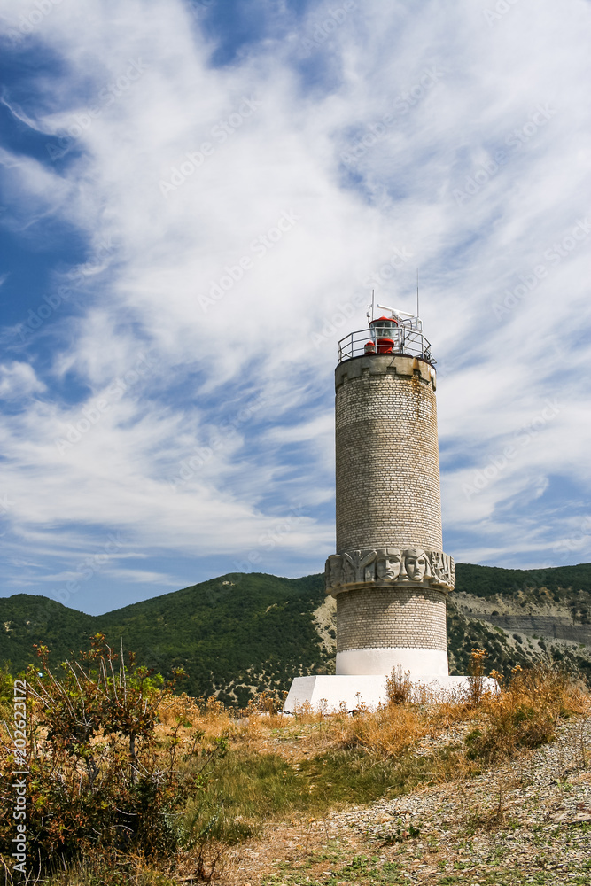 Lighthouse on the Peninsula Bolshoy Utrish, Krasnodarskiy Region, Russia against the Caucasus mountains and summer sky.