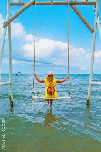 Young woman in a yellow dress is sitting on a swing.