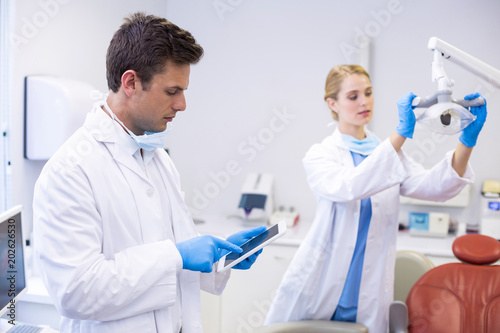 Dentist using digital tablet while his colleague adjusting dental light in background