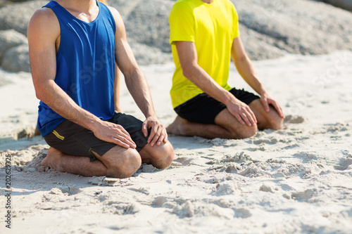 Friends in sports clothing kneeling on shore at beach