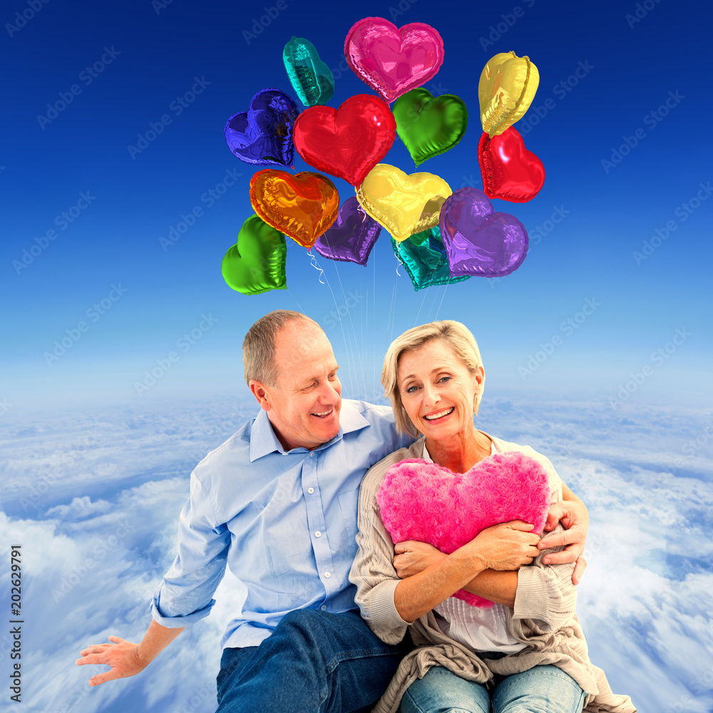 Φωτογραφία Happy mature couple with heart pillow against mountain peak through the clouds