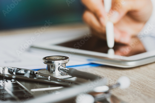 Healthcare medical concept, Blur Doctor's writing and working by stylus for order medicationon on tablet prescription online record patient at office hospital or clinic. Focus stethoscope on keybord photo