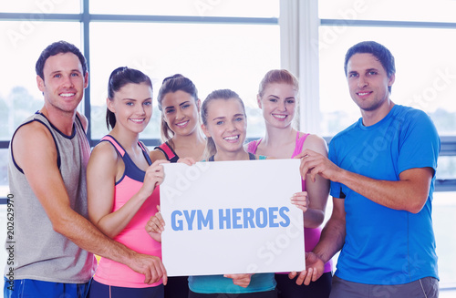 The word gym heroes against portrait of a group of fitness class holding blank paper © vectorfusionart