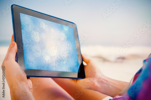 Woman sitting on beach in deck chair using tablet pc showing blue water drop pattern with circles