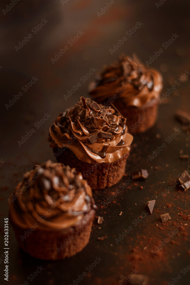 Warm photo of three homemade chocolate cupcakes on dark background. Warm photo of three homemade chocolate cupcakes on dark background.