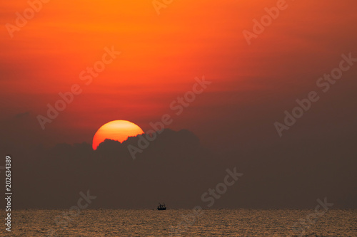 Big bright sun is rising up above the sea with little waves created the beautiful scenic of golden and red atmosphere. 