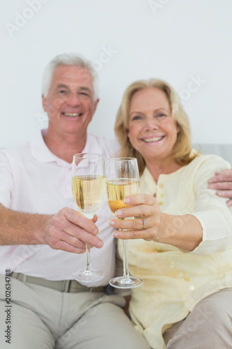 Senior couple holding out champagne flutes at home