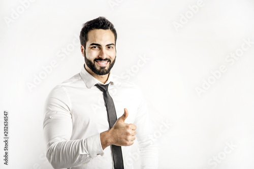 Portrait of bearded eastern man dressed in white shirt and black tie shows thumb up sign on isolated background