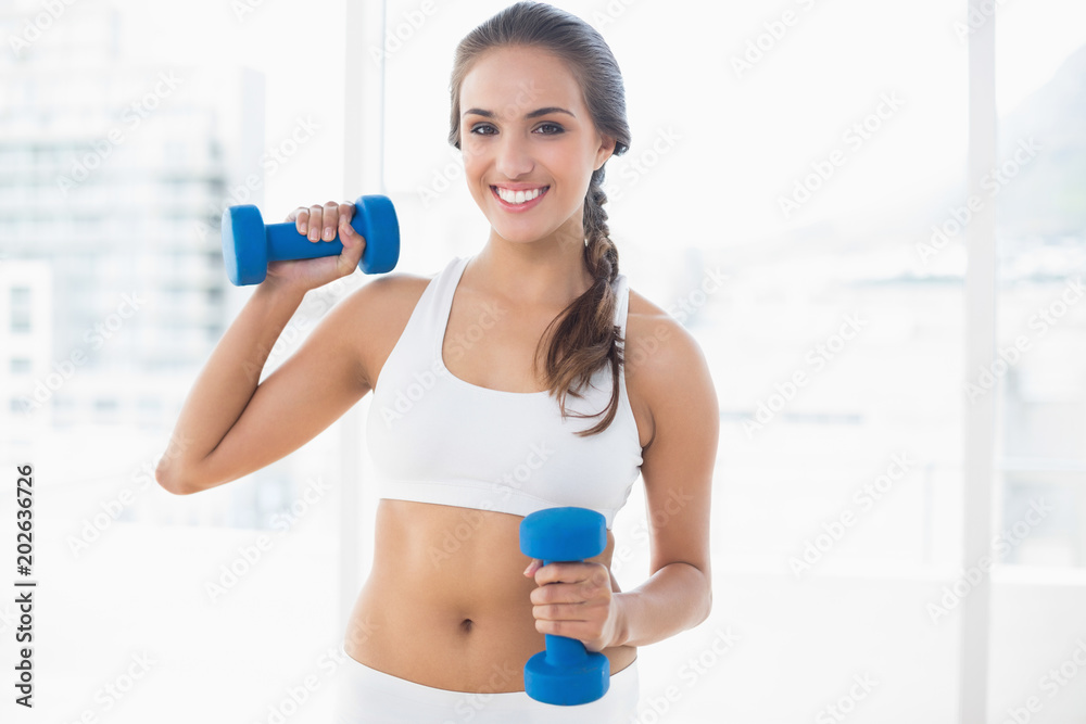 Smiling young brunette holding dumbbells