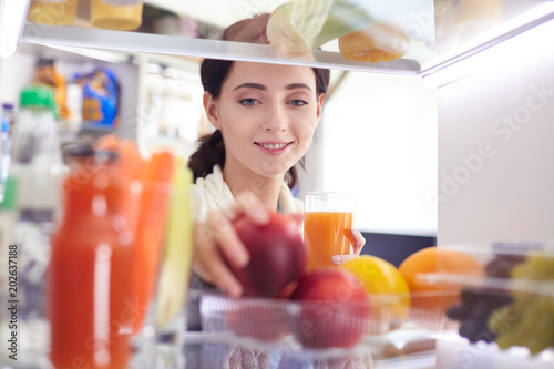 Portrait of female standing near open fridge full of healthy food, vegetables and fruits. Portrait of female