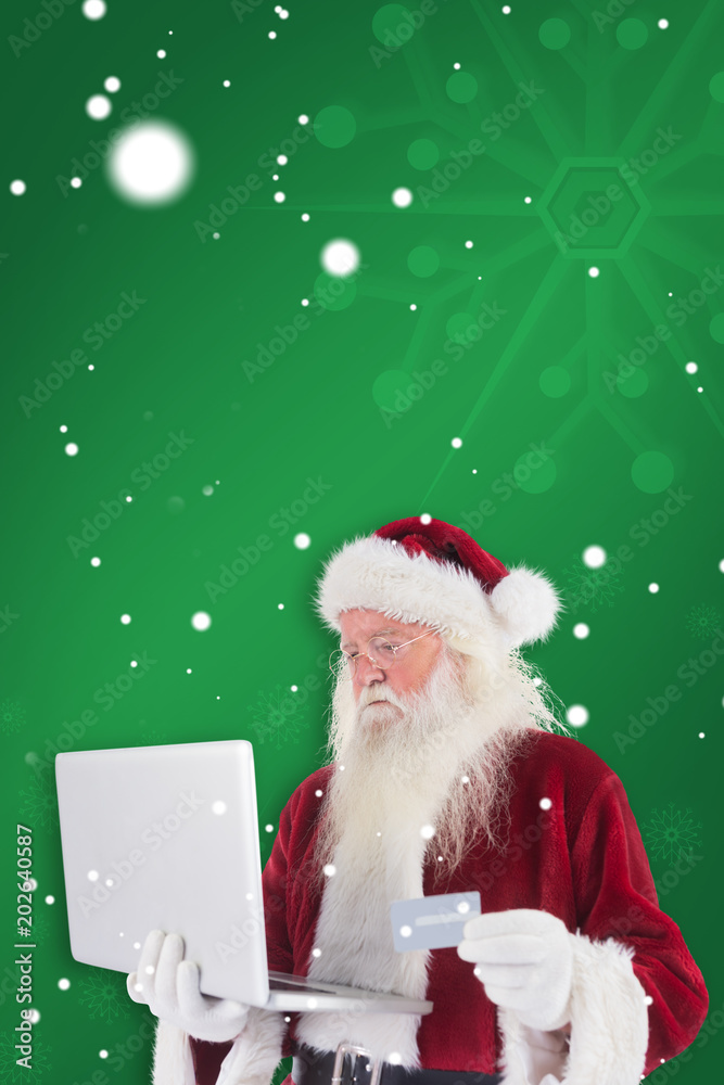 Φωτογραφία Santa pays with credit card on a laptop against green snowflake background