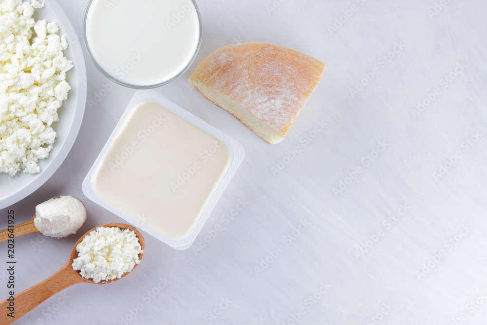 Delicious healthy dairy products on a white background: soft cheese in a white package, cottage cheese in a bowl, cream in a wooden spoon, milk in a glass. A piece of white bread. Copy space