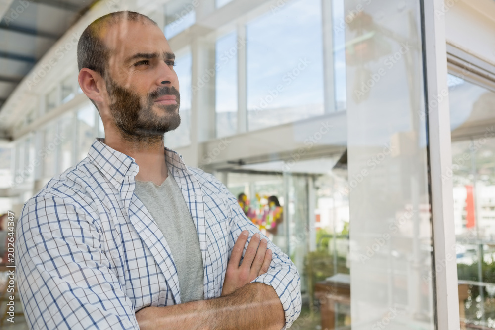 Thoughtful designer with arms crossed seen through glass Thoughtful designer with arms crossed seen through glass