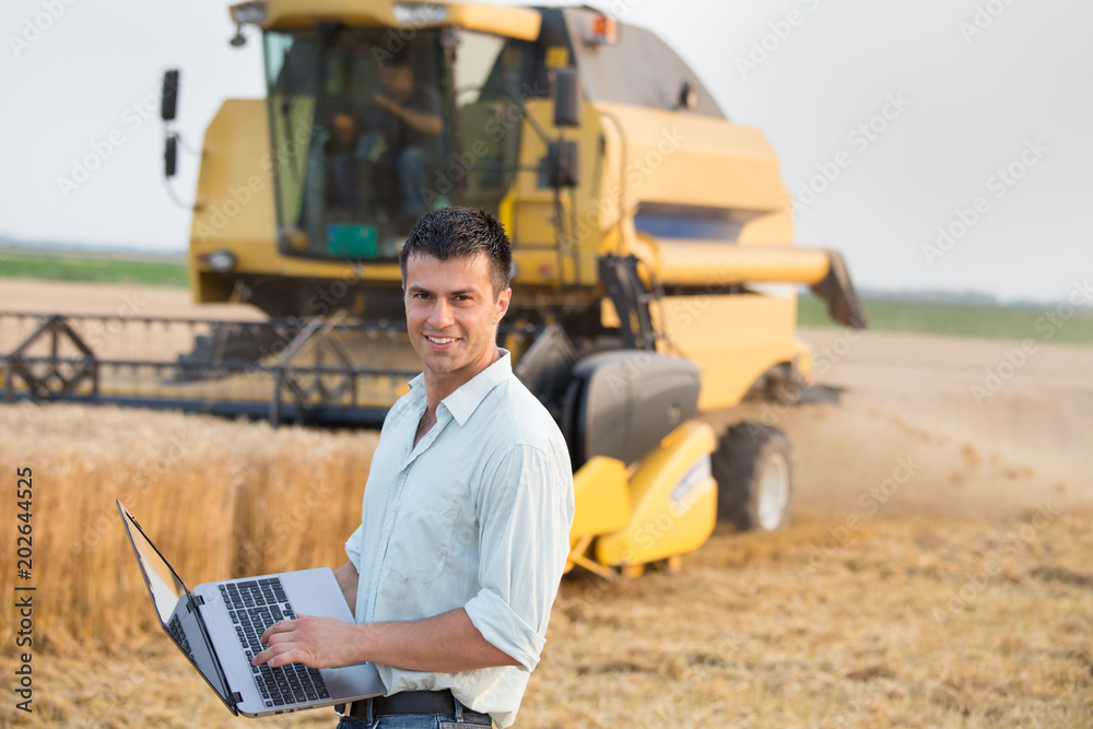 Engineer with laptop and combine harvester