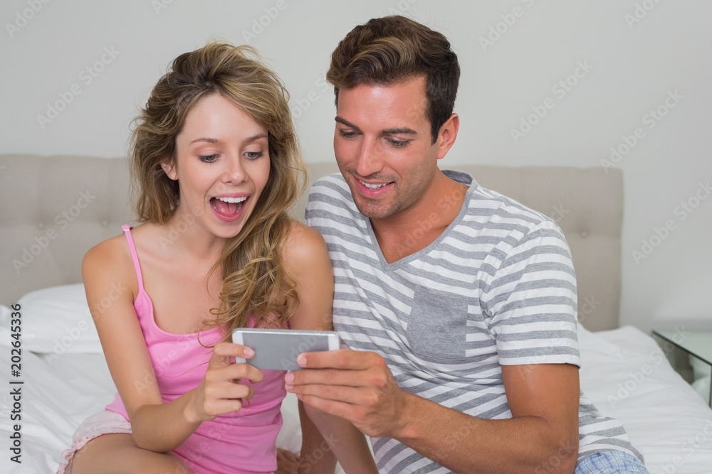 Cheerful couple reading text message in bed Cheerful couple reading text message in bed