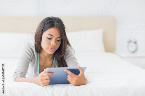 Young pretty girl lying on her bed using her tablet