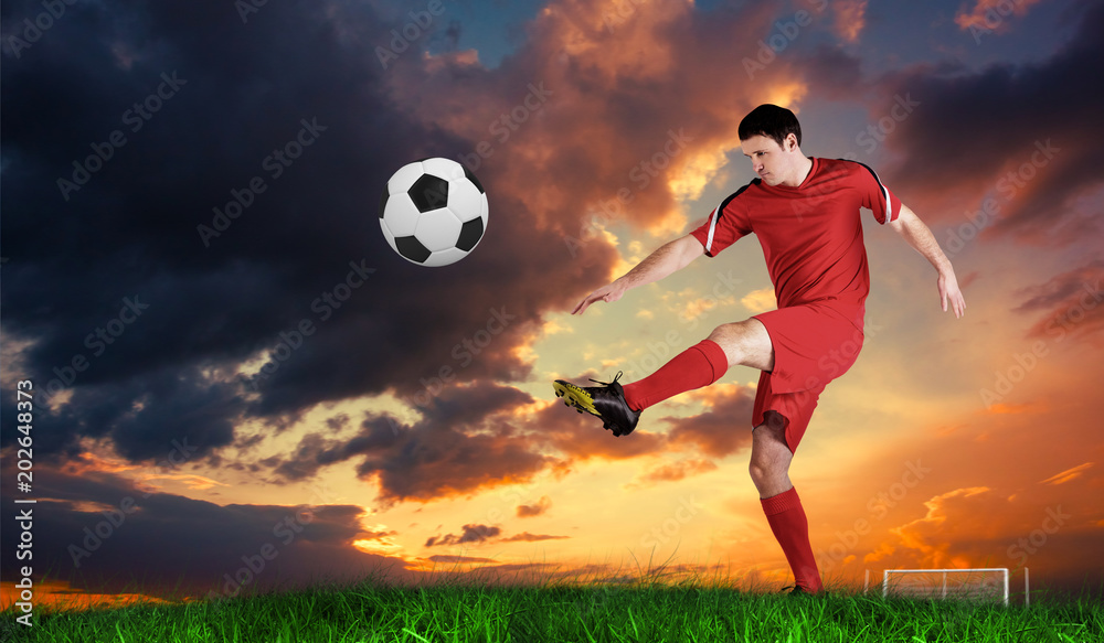Football player in red kicking against green grass under blue sky
