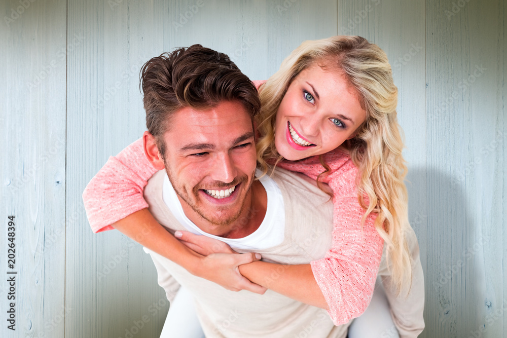 Handsome man giving piggy back to his girlfriend against wooden planks Handsome man giving piggy back to his girlfriend against wooden planks
