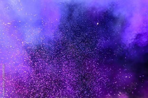 Confetti fired on air during a festival at night. Image ideal for backgrounds. Purple/magenta tonality. Smoke and lights in the middle of the multicolor confetti. Dark background as sky photo