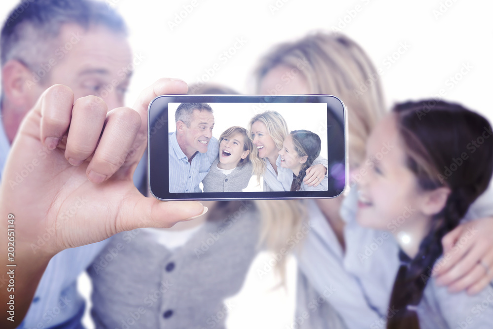 Hand holding smartphone showing against happy family with two children smiling and hugging