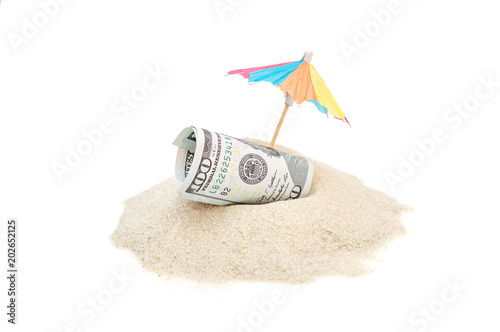 Rolled up money with beach umbrella on the heap of sand. Isolated on white.
