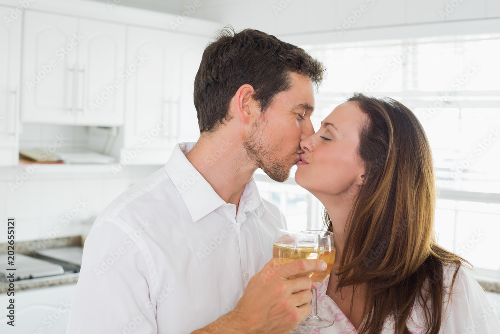 Loving couple kissing with wine glass in hand in kitchen Loving couple kissing with wine glass in hand in kitchen
