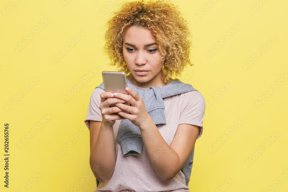 Concentrated girl is looking to the phone very accurate. Isolated on yellow background. Concentrated girl is looking to the phone very accurate. Isolated on yellow background.