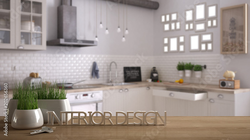 Wooden table, desk or shelf with potted grass plant, house keys and 3D letters making the words interior design, over blurred scandinavian kitchen, project concept copy space background