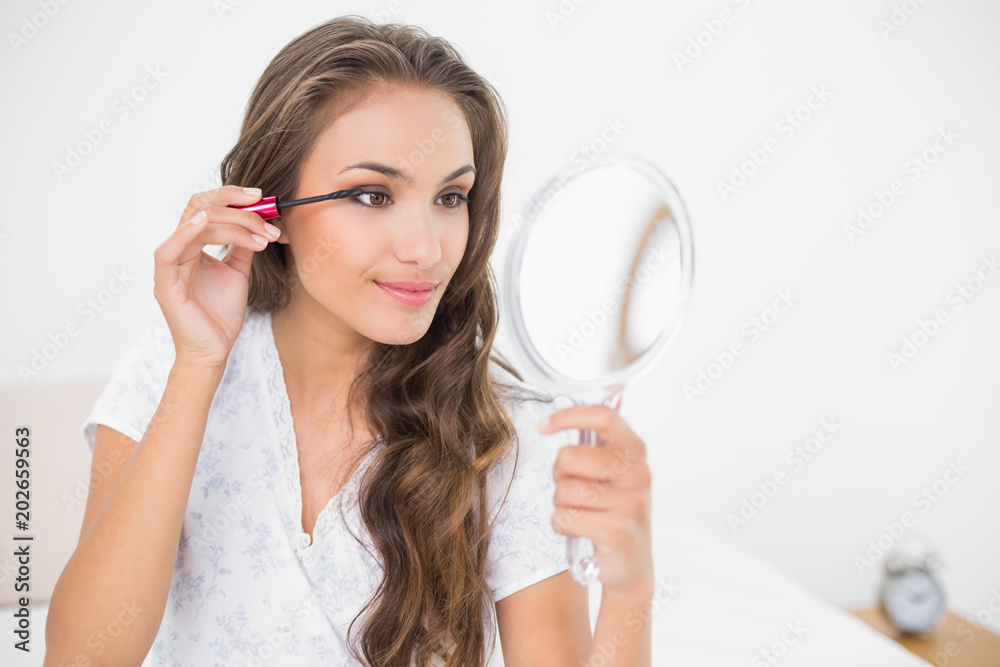 Content attractive brunette applying mascara and holding mirror Content attractive brunette applying mascara and holding mirror