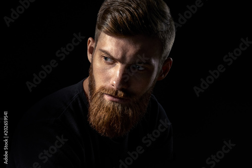 Close-up image of serious brutal bearded man on dark background Confident and dramatic concept
