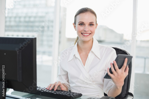 Happy businesswoman holding calculator sitting at desk